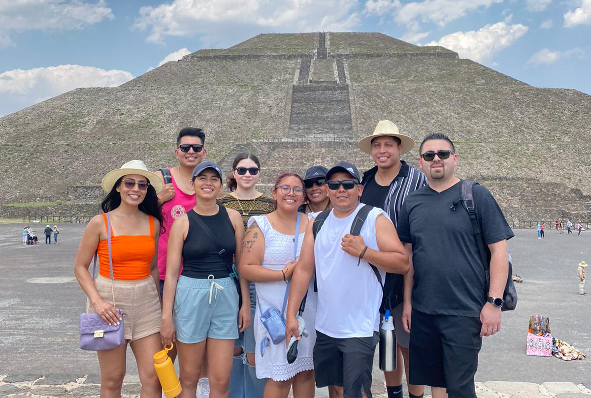 A group of people pose in front of a pyramid in Mexico.