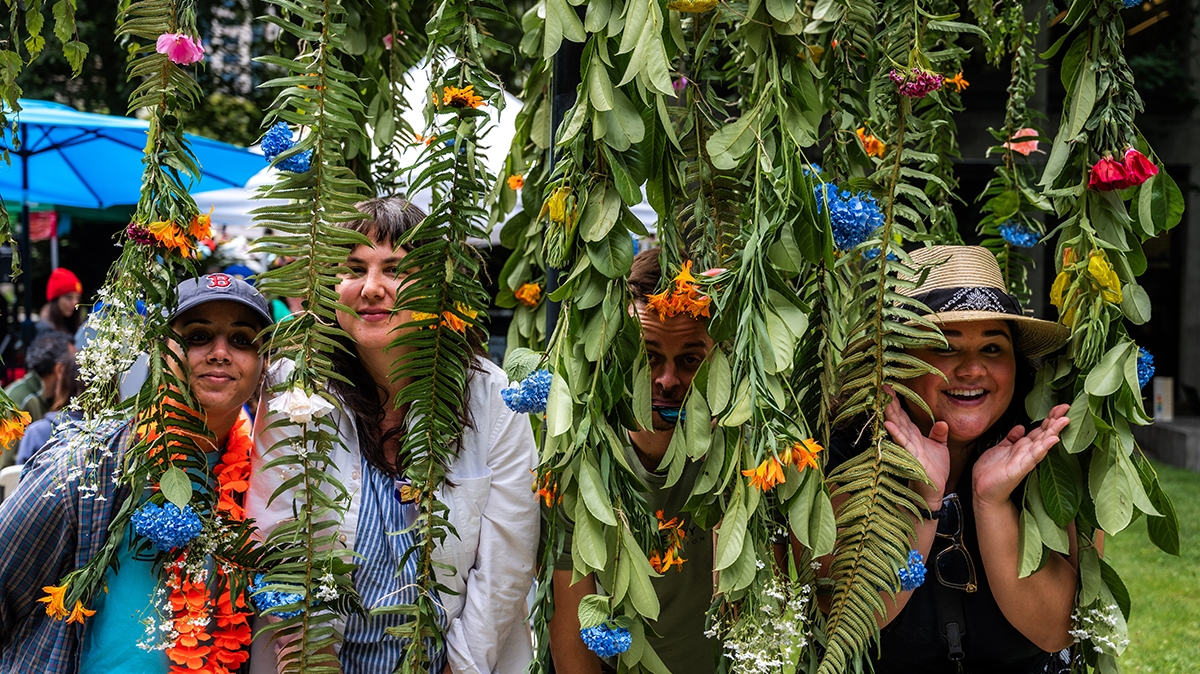 Four people peeking through hanging foliage with flowers.