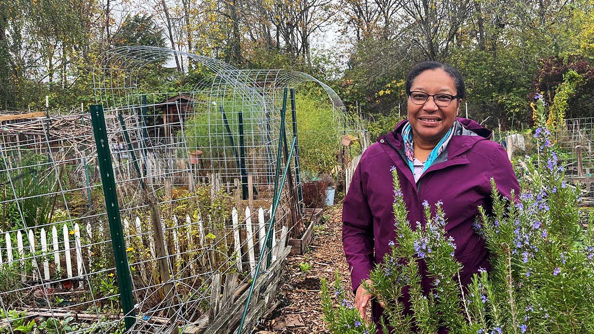 A smiling woman wearing glasses and purple jackets, stands in a garden.