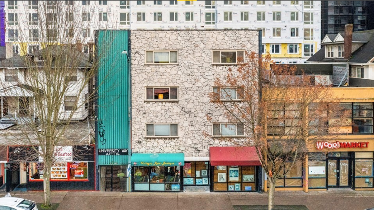 Exterior shot of an apartment building featuring six windows and turquois siding down a section on the left side and white stone on the face of most of the building.