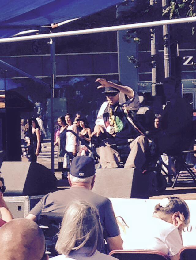 A performer in a wheelchair lifts one hand up to engage a crowd