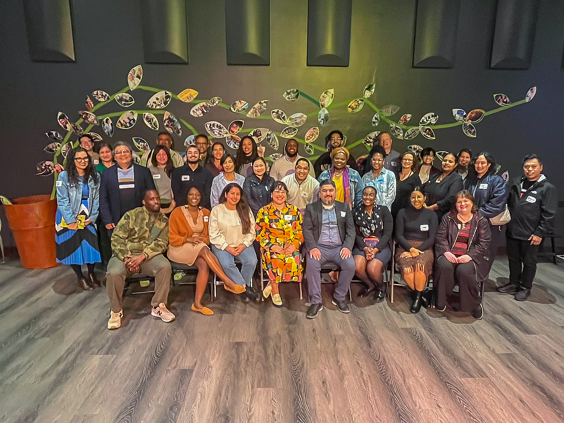 A large group of people posed together in front of a photo collage on a wall.