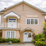 A two story, tan house with French doors on the bottom level and a porch outside of a second level door. Both doors have awnings above. A sign hanging says "Sunset Hill Community Club"