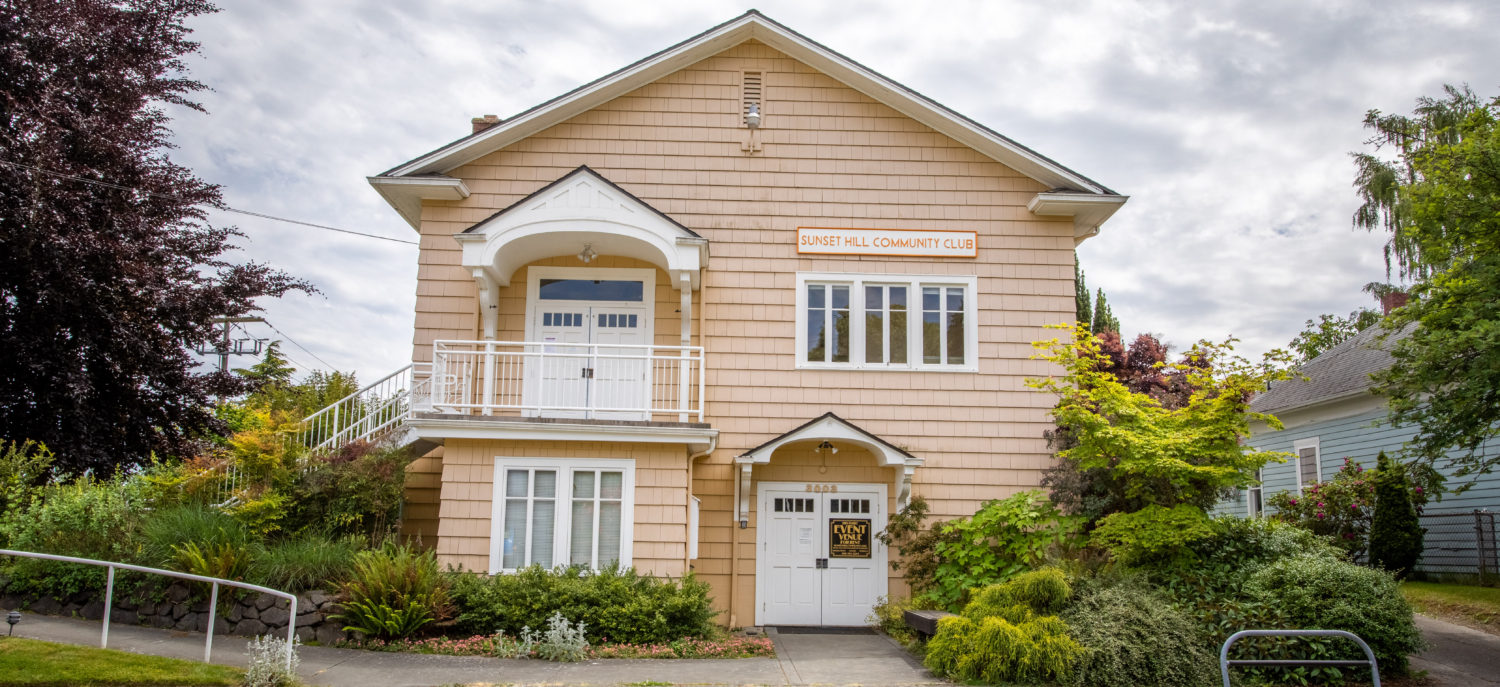 A two story, tan house with French doors on the bottom level and a porch outside of a second level door. Both doors have awnings above. A sign hanging says 