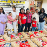 A group of nine intergenerational people stand in front of boxes of food.