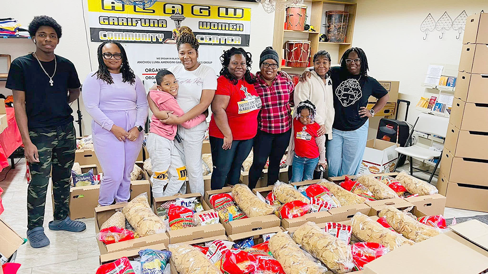 A group of nine intergenerational people stand in front of boxes of food.