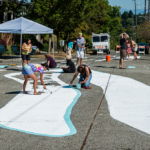 A group of people painting a large mural in the middle of a traffic intersection.