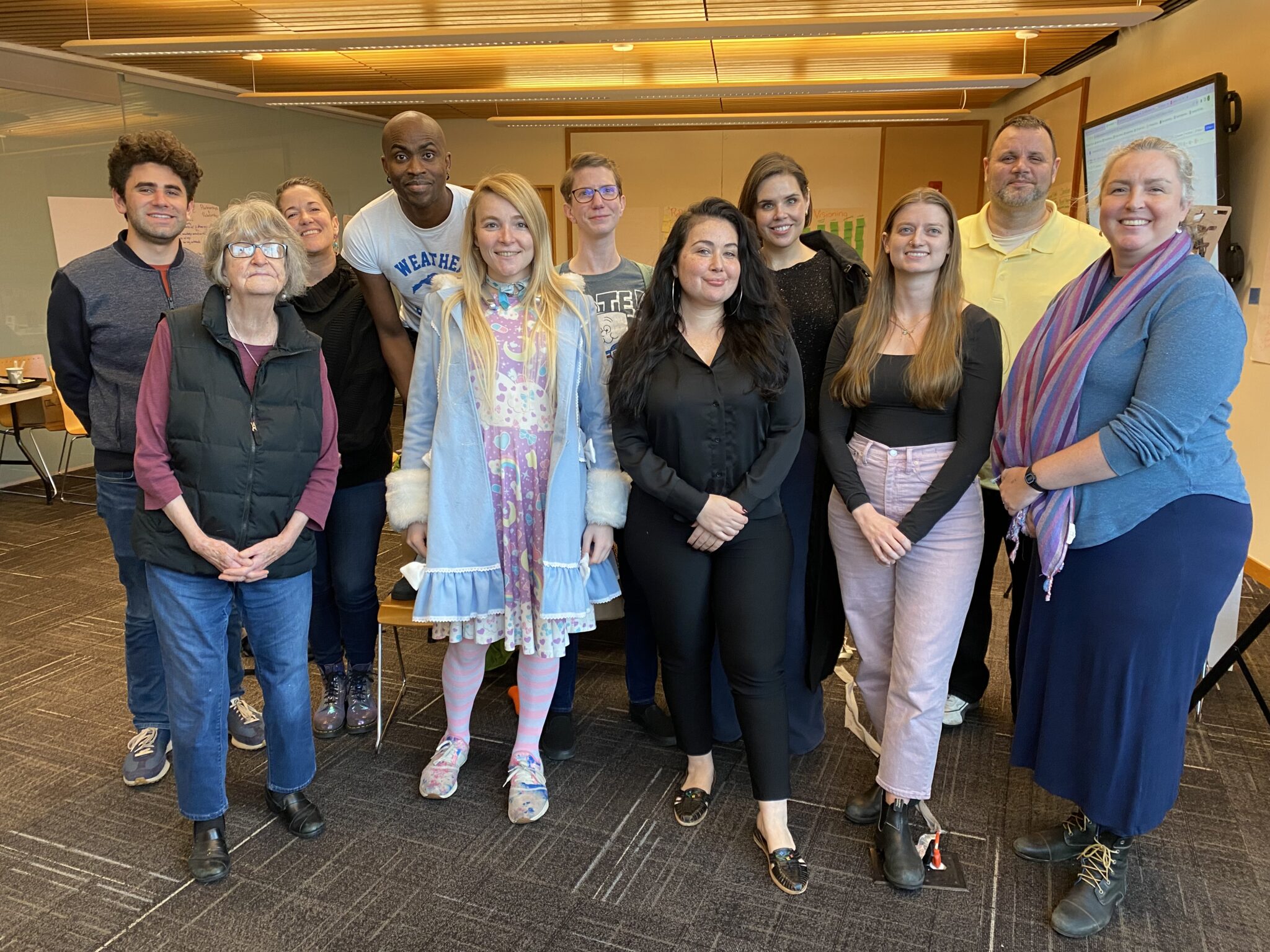 A diverse group 11 people ranging in age and ethnicity standing together smiling
