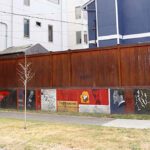 A cement wall with murals of important Black historical figures with a wood fence atop it.