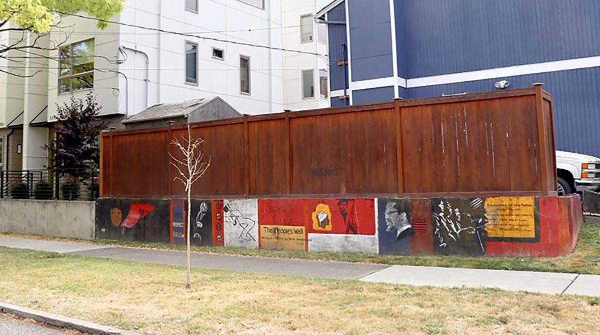 A cement wall with murals of important Black historical figures with a wood fence atop it.