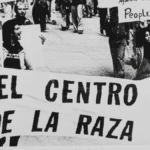 A black and white photos of people marching down the street holding a banner that says "El Centro de la Raza"