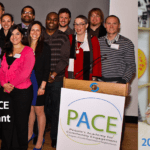 Collage of two photos; left photo includes a large group of people with text that reads "2012: Pace Participant" with an arrow pointing to a woman with long black hair. Right photo is a head shot of the same woman, 14 years later with text that reads "2026: DON Director"
