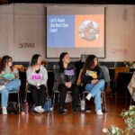 Six people sitting in chairs looking off to the right. A projector screen behind them says "Let's have the Best Day Ever!"