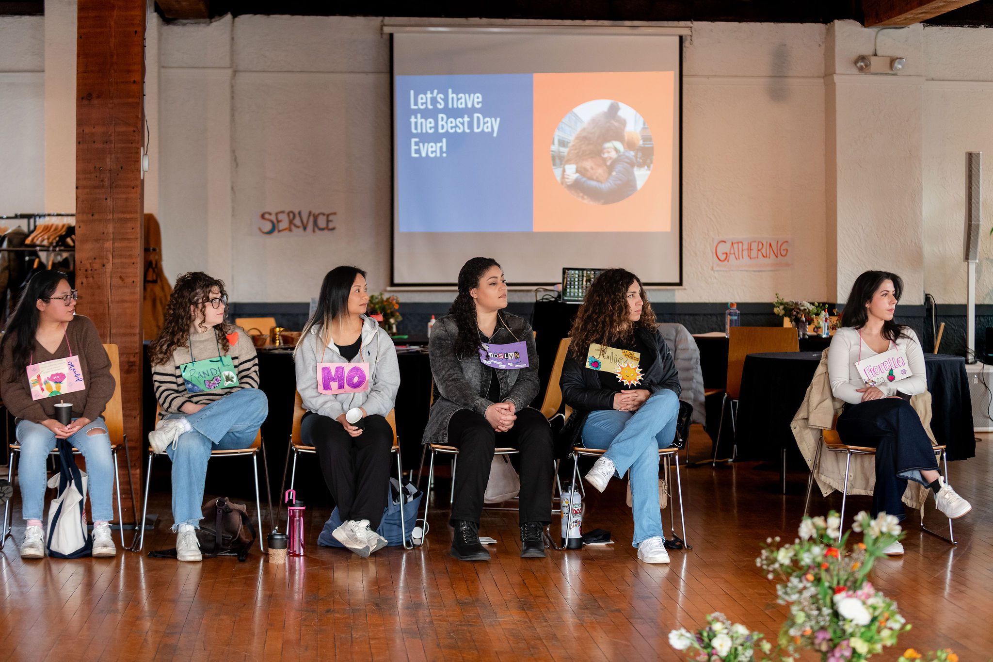 Six people sitting in chairs looking off to the right. A projector screen behind them says 
