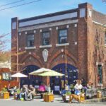 Exterior of a brick renovated firehouse with tables and landscaping in their patio hosting a party