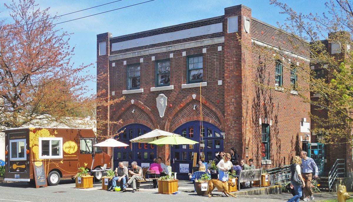 Exterior of a brick renovated firehouse with tables and landscaping in their patio hosting a party