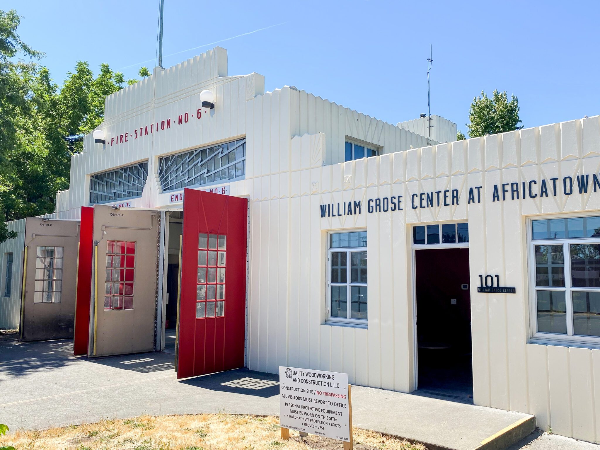 Exterior of a white building with two sets of large, red, bay doors with the words "Fire Station No 6" above them. A sign on the lower side of the building says "William Grose Center at Africatown"
