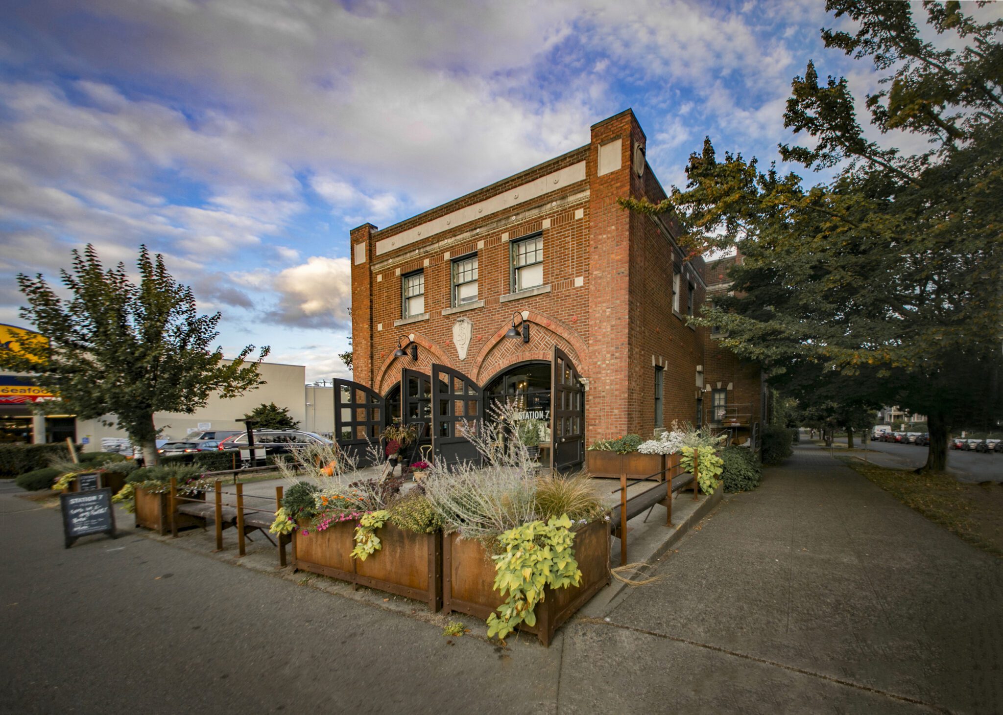 Exterior of a brick building with two large sets of bay doors open in front and a landscaped patio