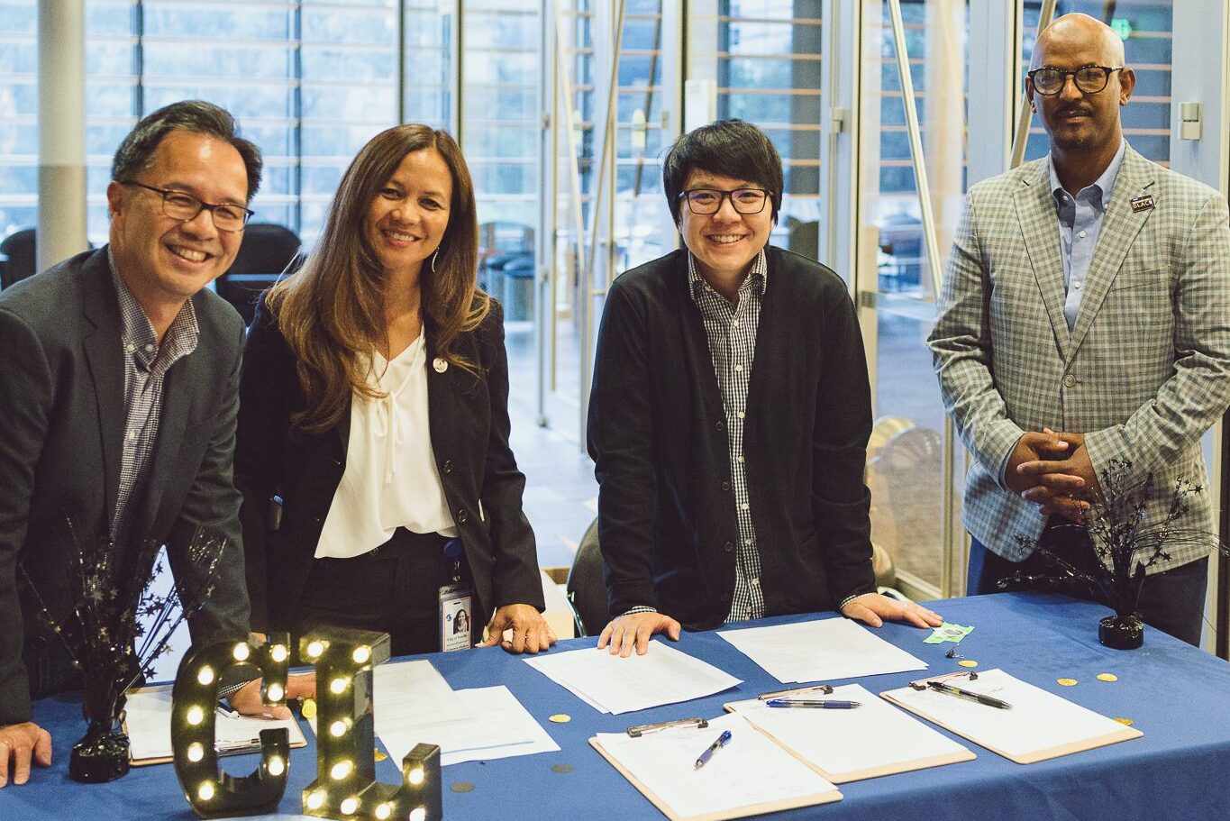 Four people standing behind a registration table with light up letters of a C and an L
