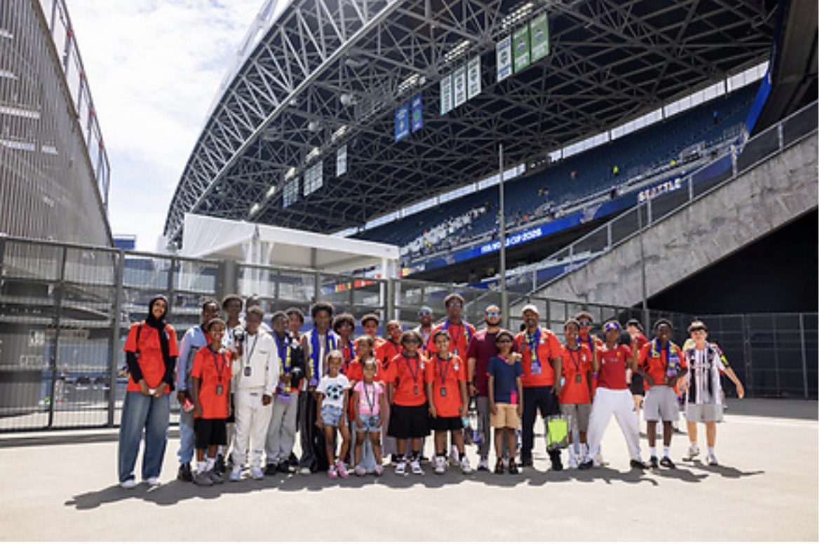 A large group of East African youth stand inside a football stadium.