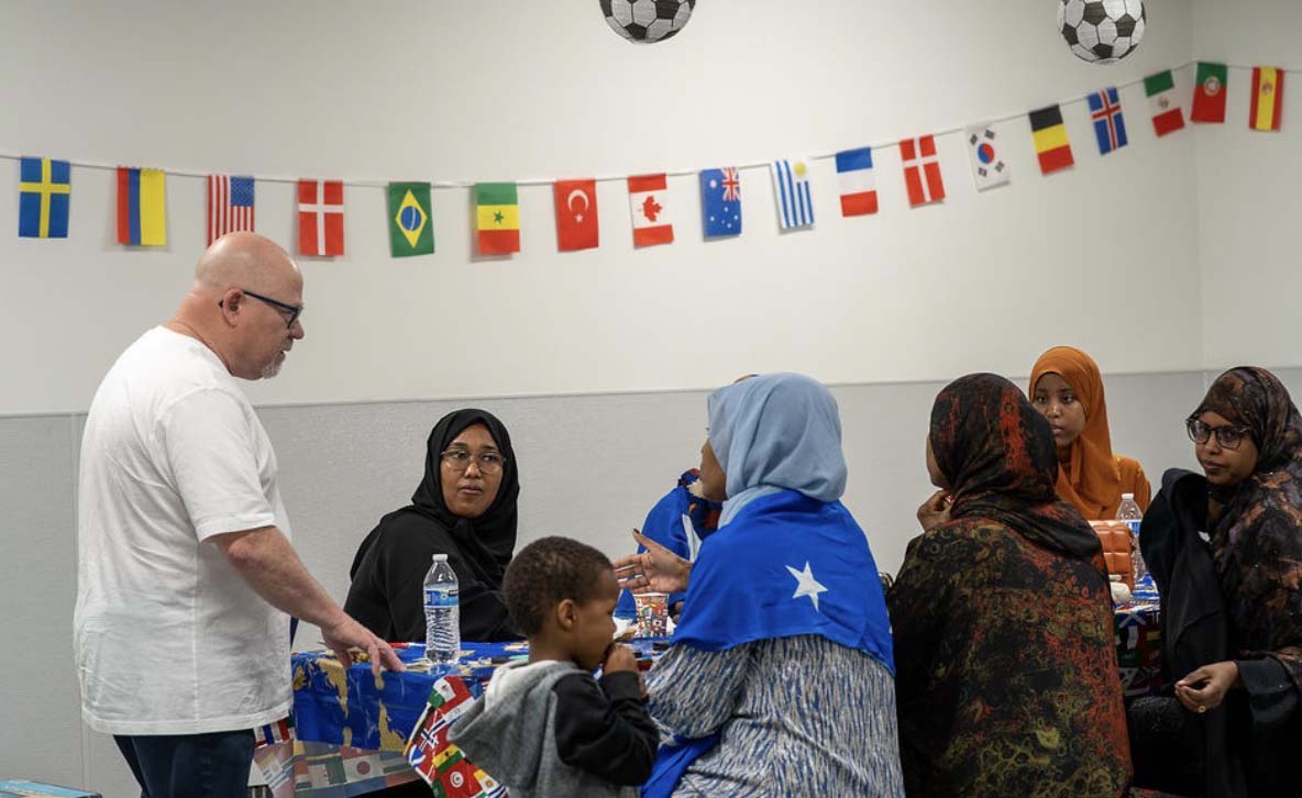 A man stands at the end of a table talking to a group of women wearing hijabs