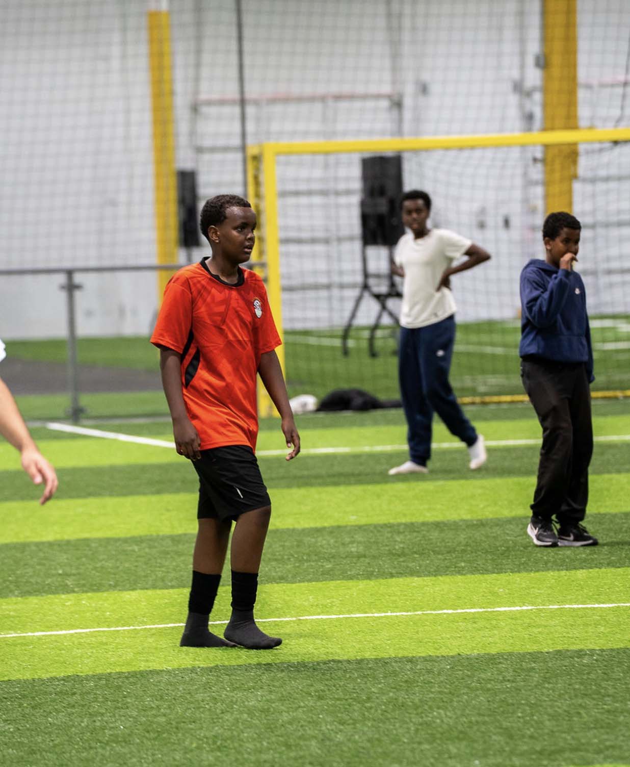 A young Somali soccer player standing on an indoor field wearing a red jersey
