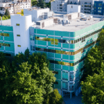 Aerial view of a six story building with rounded covers with mint green and glass wrapping the outside