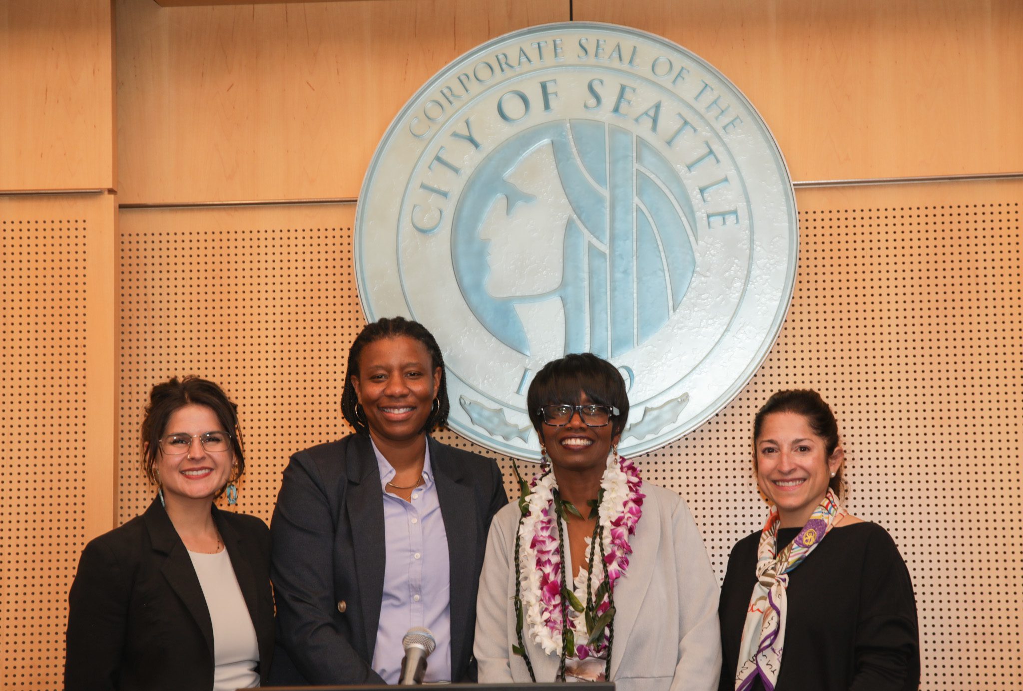 Four women standing together under the City of Seattle crest