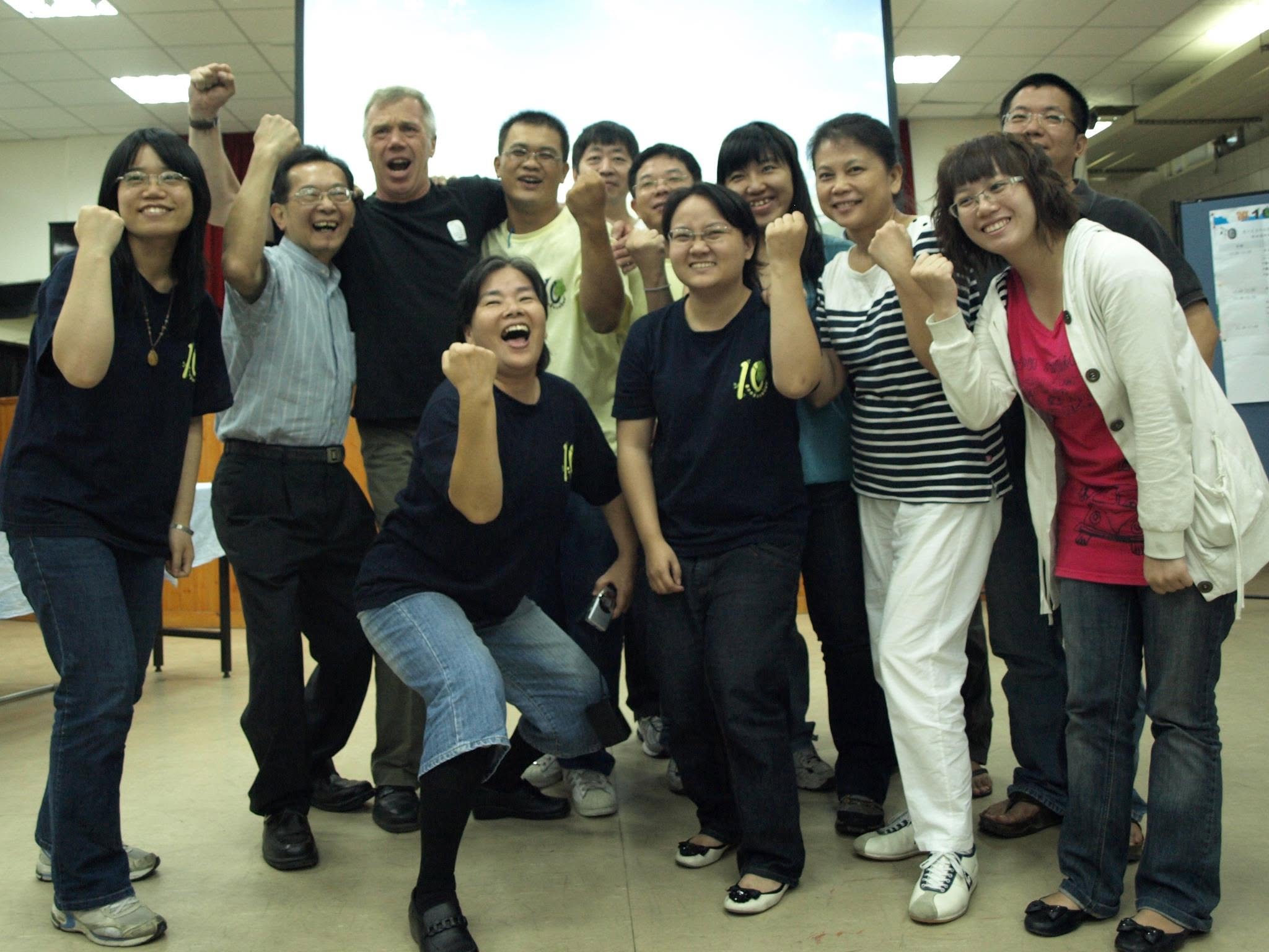 A group of people standing together in front of a projector screen holding their hands up in excitement.