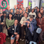 A large group of people standing together smiling in the foyer of an art gallery.