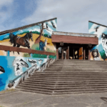 Exterior view of a building with a large staircase and murals featuring wildlife and Indigenous People