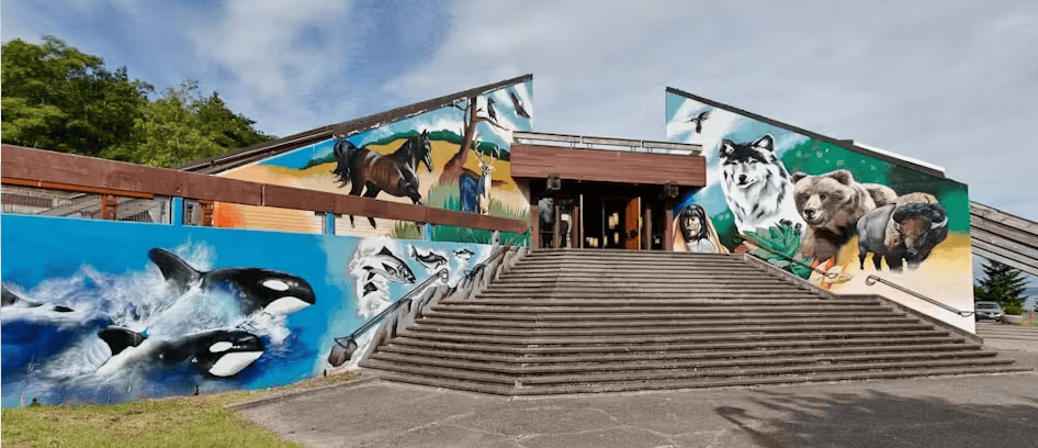 Exterior view of a building with a large staircase and murals featuring wildlife and Indigenous People