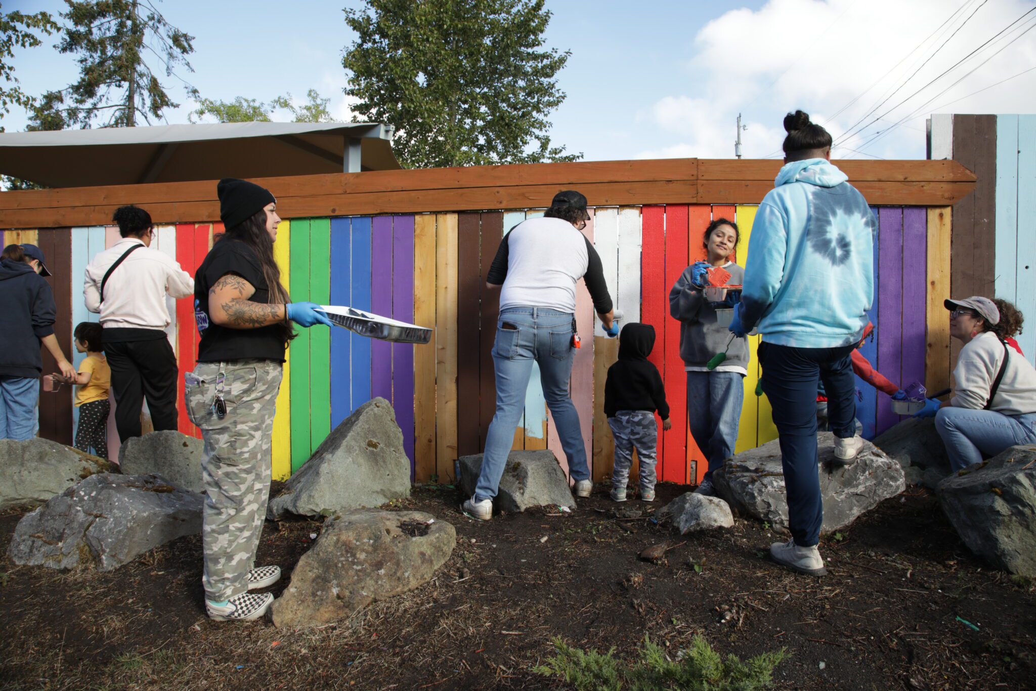 A group of people painting a wooden fence in rainbow colors