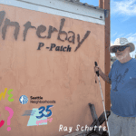 An older man with black sunglasses and a white cane standing next to a adobe pizza oven with a sign that says "Interbay P-Patch" colorful text reads: "Have We Met? Ray Schutte"